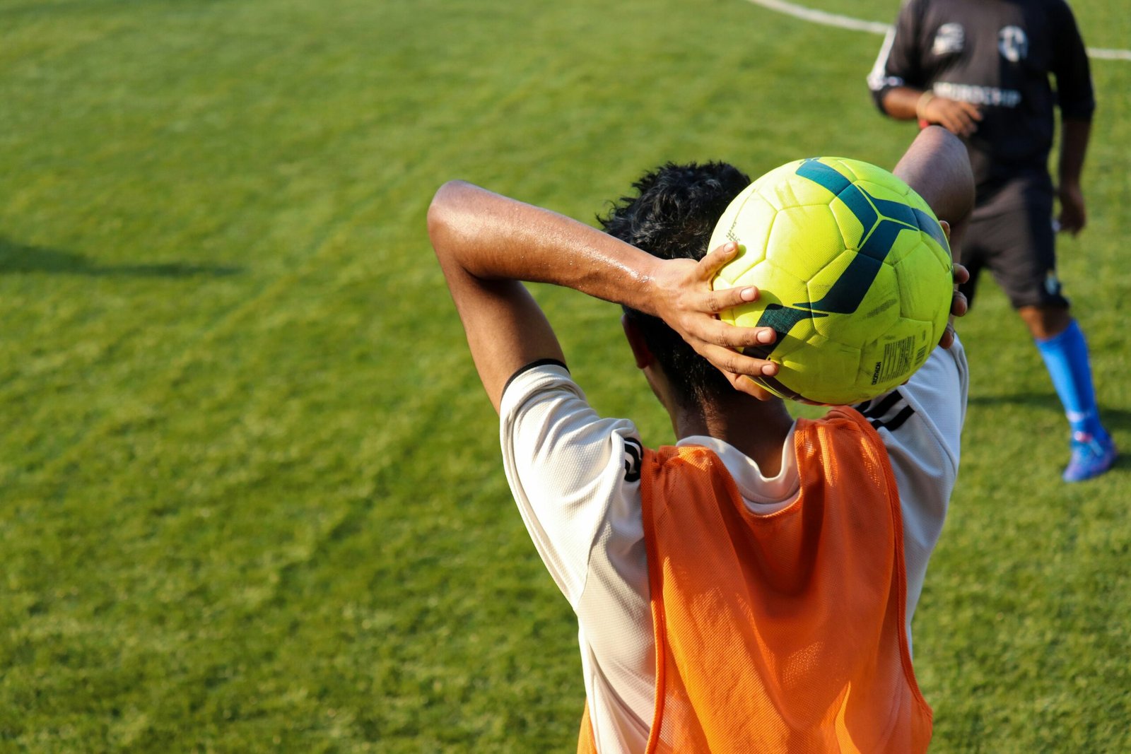 man in orange jersey shirt and white shorts holding yellow soccer ball